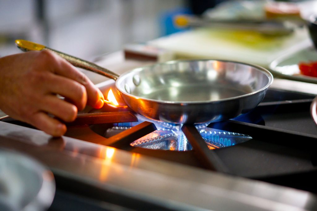 Close-up on a chef lighting up a gas stove burner with a match.
