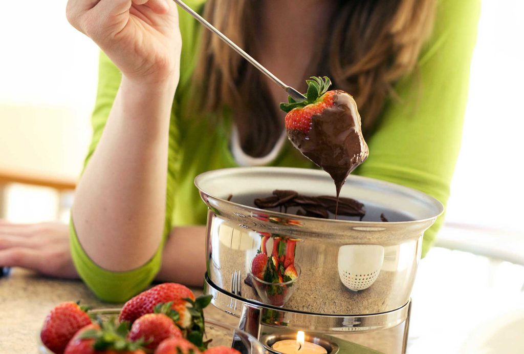 A woman pulls a strawberry from a double-boiler filled will chocolate fondue.