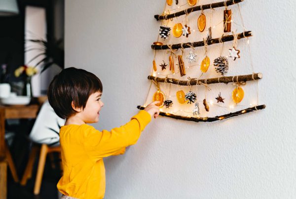 A child plays with a Christmas tree on the wall made with sticks and natural materials like dried orange slices, pine cones, etc.