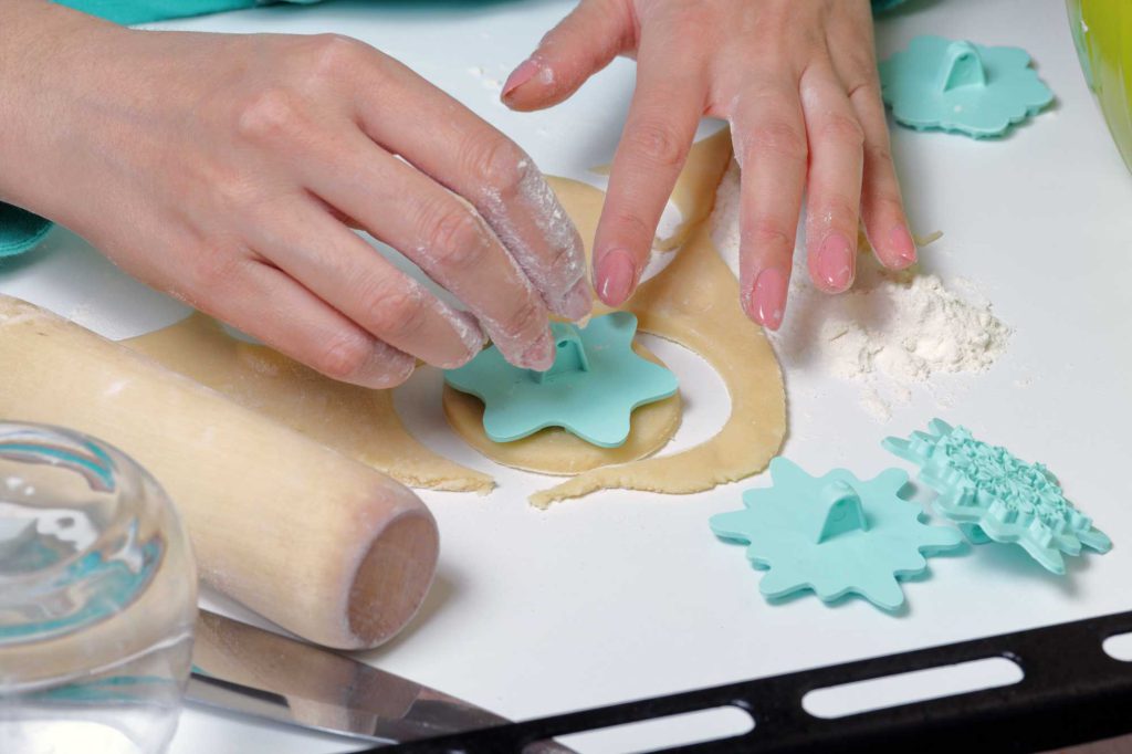 Close up on a woman's hands using a snowflake cookie cutter on some salt dough.