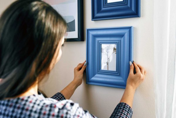 Close up of a women hanging a framed photo on the wall.